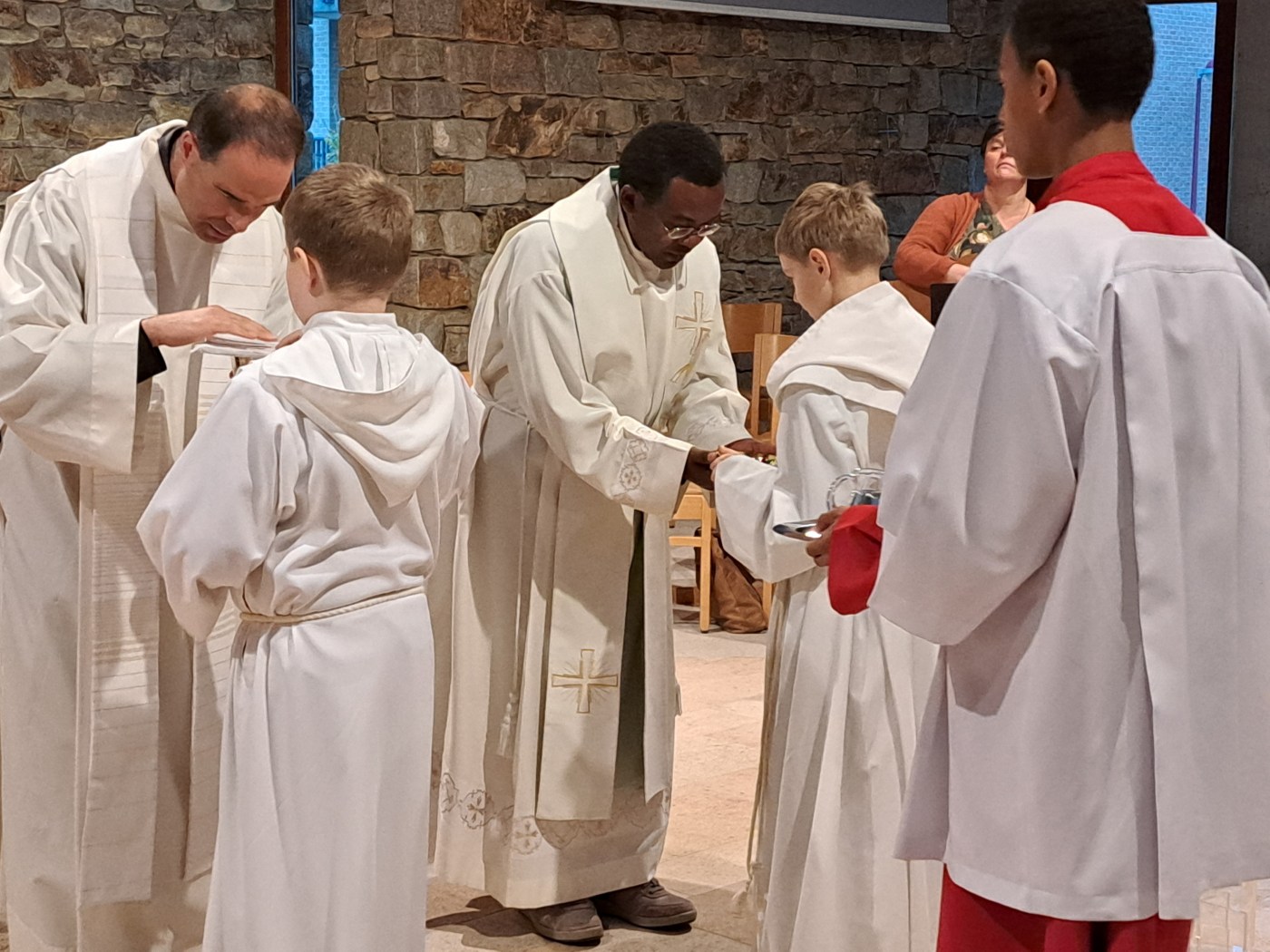 Nous voyons deux prêtres qui reçoivent l'un le calice, l'autre la patène avec le pain que leur apportent deux acolytes habllés en aube blanche. Derrière les deux acolytes, un troisième acolyte, habillé avec un aube rouge et un surplis blanc, apporte sur un plateau les burettes qui contiennet le vin et l'eau.